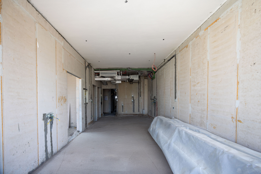 Cove Edition I By Imtiaz 1 An interior view of an unfinished room with bare walls, exposed wiring, and construction materials scattered.
